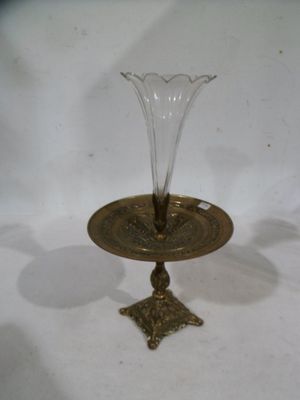 un vase en verre posé sur une plaque en laiton sur une surface blanche
