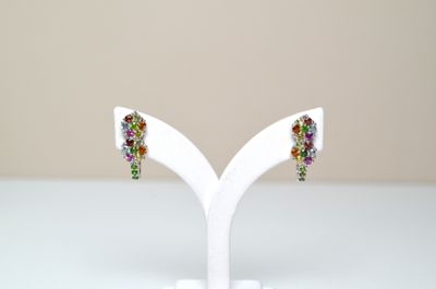 une paire de boucles d'oreilles multicolores posées sur un présentoir blanc, sur une table blanche