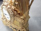 a gold clock sitting on a table with a woman on it