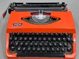 une machine à écrire orange posée sur une table, à côté d'un clavier