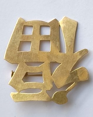 une broche en or sur laquelle figurent des caractères chinois sur un fond blanc
