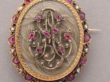 an image of a gold and ruby broochle with a monogram on it