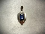 a pendant with a blue stone in it on a white surface