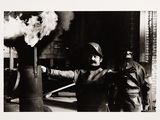 black and white photograph of a man holding a fire extinguisher in front of a fire hydrant