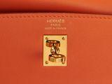 the handle of an orange leather handbag with gold hardware