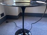 une table en verre avec un piètement noir, sur laquelle est posé un vase blanc