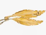 two gold leaf brooches on a white background