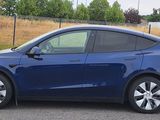 La Tesla Model Y est garée sur un parking près d'un champ.