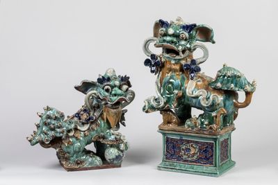 une paire de statuettes « foo foo » bleues et vertes posées sur des socles, sur fond blanc