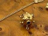 a gold necklace with a frog on it on a wooden table