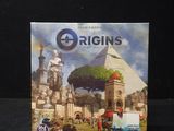 une image représentant une boîte du jeu de société « Origins » posée sur une surface noire