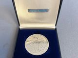 une photo d'une médaille d'argent dans un écrin bleu