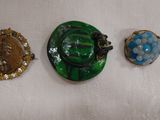 Trois broches de couleurs différentes sont exposées sur un fond blanc