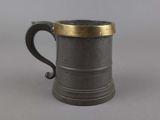 an old pewed mug with a gold rim sits on a gray surface