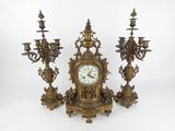 une horloge posée sur une table à côté de trois chandeliers