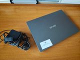 L'ordinateur portable Asus est posé sur une table en bois, à côté d'un chargeur.