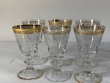 four wine glasses with gold rims are lined up on a table