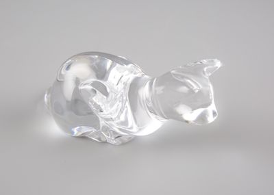 une figurine en verre représentant un chat posée sur une surface blanche