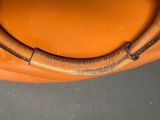 an orange leather bag with a metal handle on top of a table