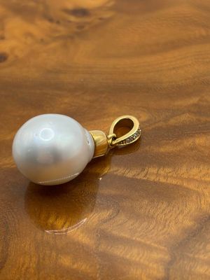 pendentif en perle posé sur une table en bois, muni d'une chaîne en or