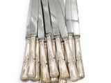 six silverplated knives and a knife holder on a white surface