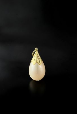 a gold pendant with a pearl on a black background