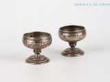 two silver cups sitting next to each other on a white surface