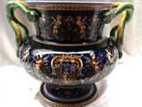 un grand vase bleu muni d'une anse verte, posé sur un socle