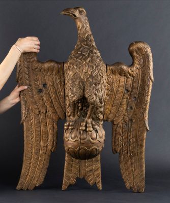 une femme tient dans ses mains une grande sculpture en bois représentant un aigle