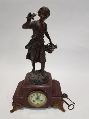 une statue en bronze représentant une femme tenant un panier de fleurs au sommet d'une horloge