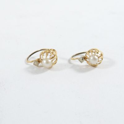 une paire de boucles d'oreilles en perles et en or posées sur une surface blanche