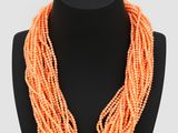 un collier composé de perles orange et muni d'un fermoir doré, posé sur un mannequin
