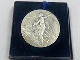 une image représentant une médaille d'argent ornée d'un ruban bleu, posée sur un coffret noir