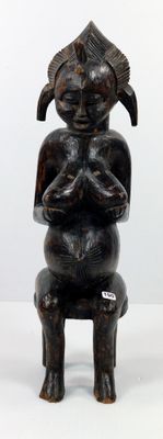 une statue en bois représentant une femme assise sur un tabouret
