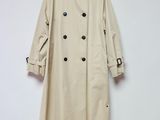 un trench-coat beige accroché à un mur blanc