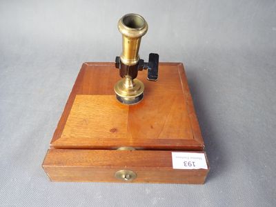 un microscope ancien plaqué laiton, présenté dans un coffret en bois, posé sur une surface grise