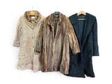 three coats of fur hang on a clothes rack against a white wall