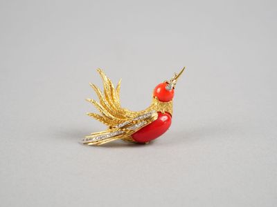 une broche en forme d'oiseau, dorée et rouge, sur un fond blanc