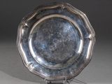 un plat ancien en argent posé sur un socle, sur fond gris