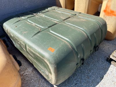 une valise verte posée par terre à côté de quelques fûts