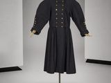 une photo d'une robe noire ornée de boutons dorés, présentée sur un mannequin