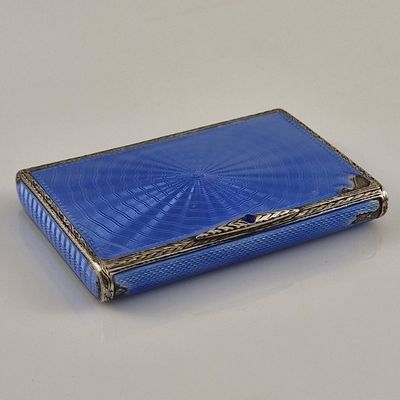 un étui à cigarettes ancien en argent et verre bleu posé sur une surface blanche