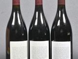 three bottles of red wine are lined up on a table