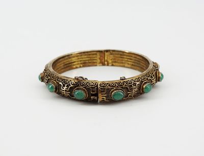 a gold bracelet with green stones on a white background