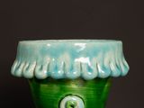 a green vase with a button on it on a table