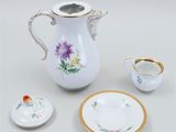 a white pitcher with flowers on it next to a cup and saucer