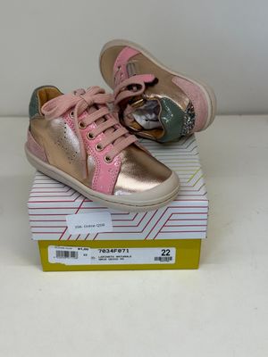 une paire de chaussons de bébé roses et dorés posés sur une boîte, sur une surface blanche