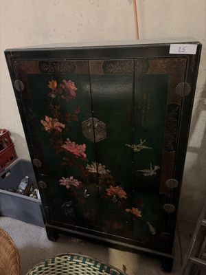 a black cabinet with flowers painted on it and a basket on the floor