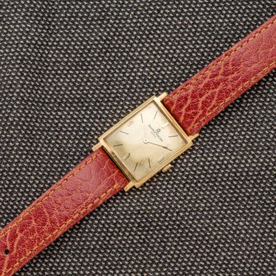 un gros plan d'une montre posée sur une surface noire, avec un bracelet rouge
