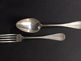 two silver spoons and a fork on a black surface